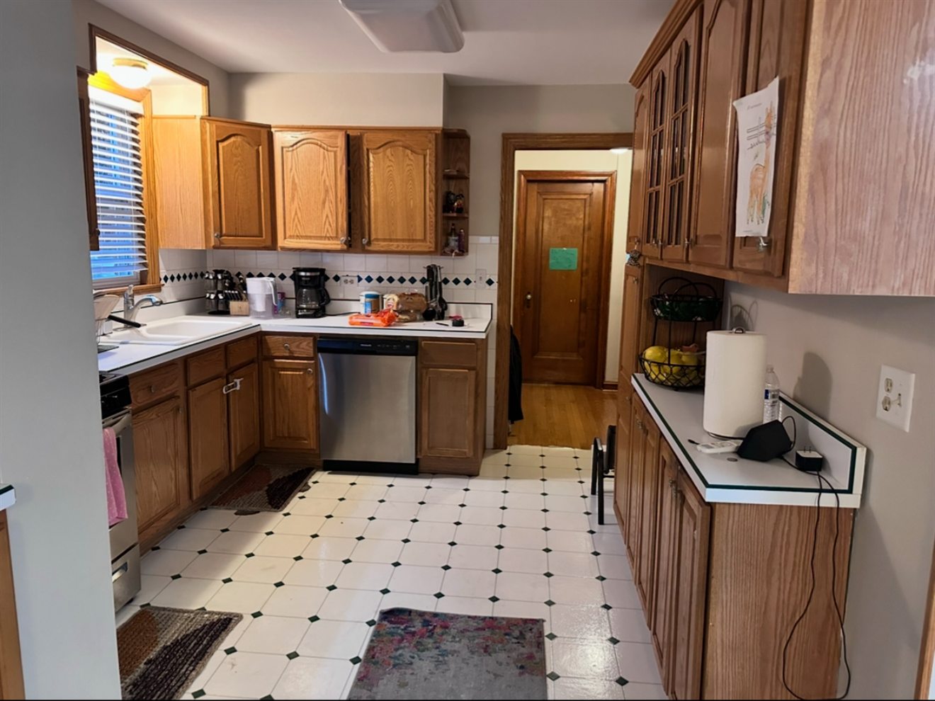 The same kitchen before: oak cabinets, white laminate counters, and black and white vinyl tile floors.
